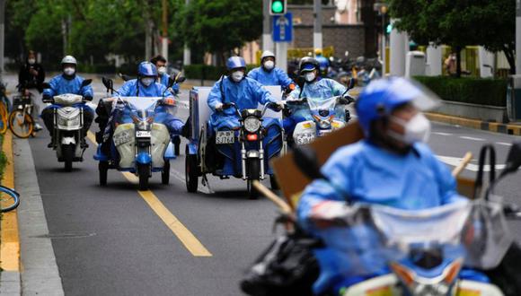 Trabajadores con trajes protectores montan triciclos y scooters eléctricos durante el encierro, en medio de la pandemia de la enfermedad por coronavirus (COVID-19), en Shanghái, China.
