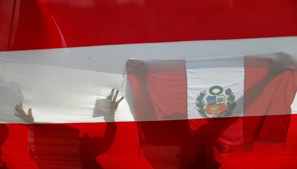 Los reservistas del ejército peruano se ven a través de una bandera peruana mientras sostienen banderas peruanas durante una "marcha por la democracia" cerca del edificio del Congreso en Lima el 17 de noviembre de 2020. (Foto por Luka GONZALES / AFP)