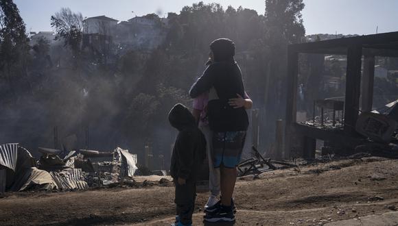 Una familia observa casas destruidas por un incendio el 23 de diciembre de 2022, en cerro Forestal, en Viña del Mar, Chile. (Foto de Adriana Thomasa / EFE)
