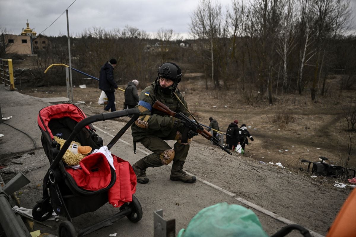 A Ukrainian serviceman takes cover as people evacuate the city of Irpin on March 13, 2022. (ARIS MESSINIS / AFP)