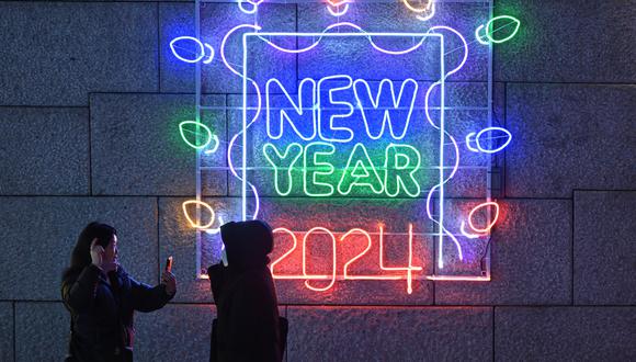 La gente toma fotografías frente a una pantalla de luz que dice "Año Nuevo 2024" en el centro de Seúl el 22 de diciembre de 2023. (Foto referencial, Jung Yeon-je / AFP).