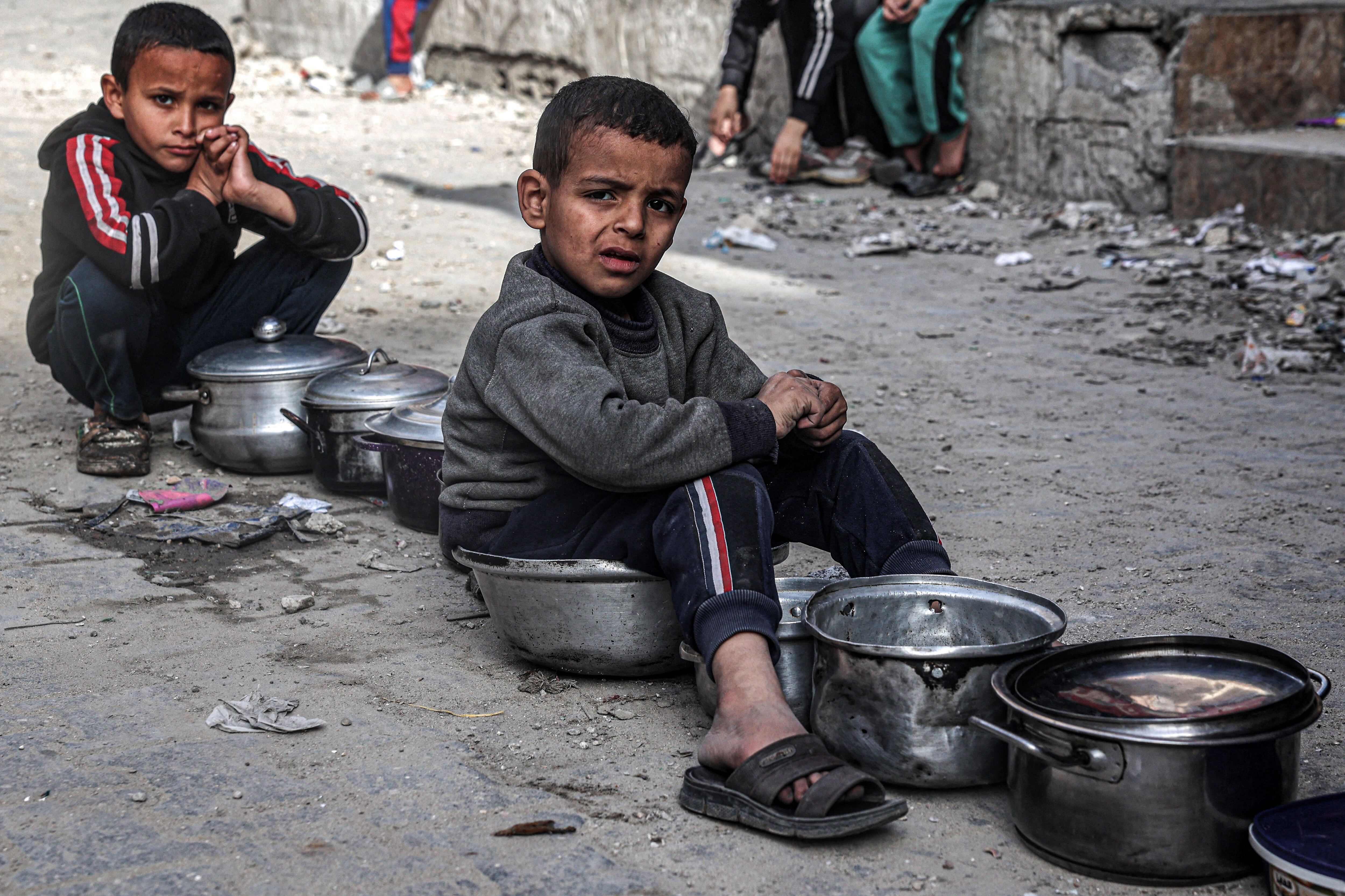 Children sit with empty pots as displaced Palestinians line up to receive food provided by a charity in Rafah, southern Gaza Strip, March 16, 2024. (Photo by SAID KHATIB/AFP).