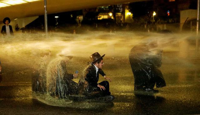Israeli ultra-Orthodox Jewish men sit as a water canon is activated during a protest against the detention of a member of their community who refuses to serve in the Israeli army, in Jerusalem March 8, 2018. REUTERS/Ronen Zvulun     TPX IMAGES OF THE DAY
