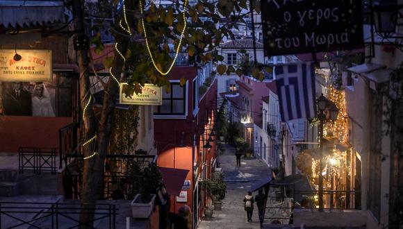 La gente pasa frente a negocios y restaurantes cerrados en la zona turística de Plaka, en Atenas, Grecia, el 13 de enero de 2021, en plena pandemia de coronavirus. (LOUISA GOULIAMAKI / AFP).