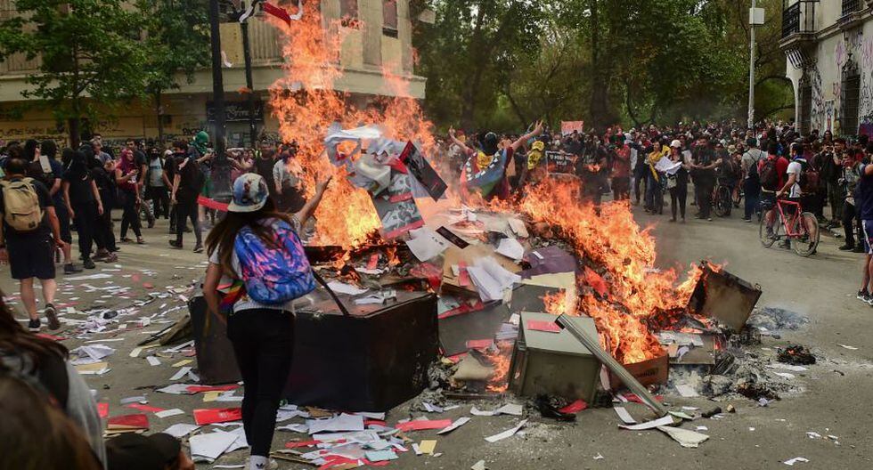 Los manifestantes queman documentos y objetos después de saquear una sucursal de un banco en Santiago. (Foto: AFP).