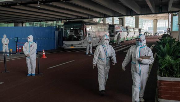 Los trabajadores de la salud con trajes de protección personal caminan junto a los autobuses en una sección acordonada en el área de llegadas internacionales del aeropuerto internacional de Wuhan el 14 de enero de 2021. (Foto de NICOLAS ASFOURI / AFP).