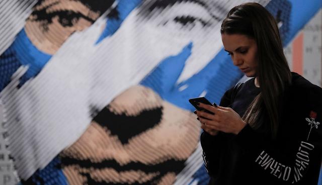 A woman looks at a mobile phone as she stands in front of a painting depicting Russian president Vladimir Putin at the "SUPERPUTIN" exhibition in UMAM museum in Moscow, Russia, December 6, 2017. REUTERS/Maxim Shemetov  NO RESALES. NO ARCHIVES