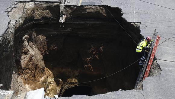 Un rescatista baja una escalera hacia un agujero gigante en una carretera, causado por el colapso de un sistema de drenaje debido a las fuertes lluvias que azotaron el país, en Villa Nueva, 15 km al sur de Ciudad de Guatemala, el 25 de septiembre de 2022. (Foto por Johan ORDONEZ / AFP)