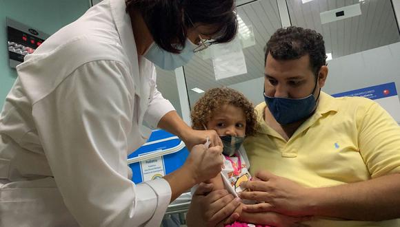 Pedro Montano sostiene a su hija Roxana Montano, de 3 años, mientras es vacunada contra el coronavirus COVID-19 con la vacuna cubana Soberana Plus, el 24 de agosto de 2021 en un hospital de Cuba. (ADALBERTO ROQUE / AFP).