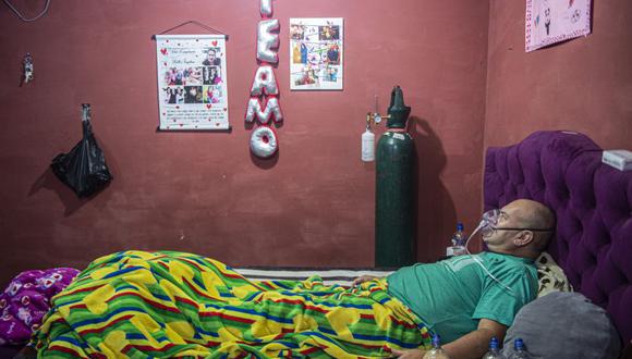 El venezolano Wilmer Hernández, de 44 años, respira ayudado por un tanque de oxígeno en su habitación en el barrio de Villa María del Triunfo, al sur de Lima, el 25 de junio de 2020. Catorce miembros de la familia Hernández llegaron a Perú desde Venezuela hace dos años, pero el el coronavirus ha puesto a prueba sus esperanzas de una vida mejor: el abuelo murió y los otros 13 están tratando de sobrevivir a la enfermedad. (Foto: ERNESTO BENAVIDES / AFP).