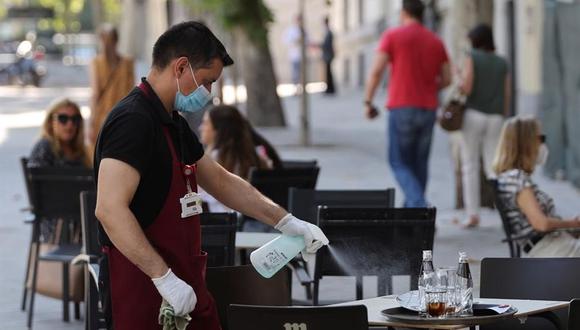 Un camarero desinfecta una mesa tras las marcha de los clientes de la terraza de un bar del centro de Madrid. La Comunidad de Madrid declaró obligatorio el uso de mascarilla en todos los espacios, abiertos o cerrados para frenar el rebrote de coronavirus en España. (EFE/Mariscal).