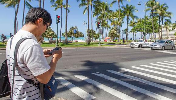Una persona mira su celular antes de cruzar en una esquina de Honolulu, Hawaii. (Foto: AFP)