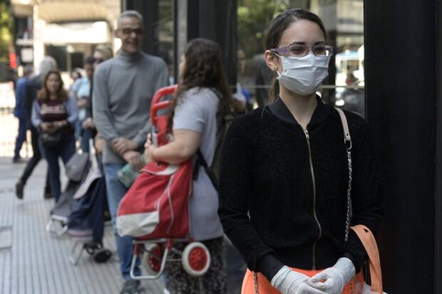 Una mujer con máscara quirúrgica y guantes de látex hace cola para ingresar a un supermercado durante el brote del nuevo Coronavirus, COVID-19, en Buenos Aires (Foto: Juan Mabromata / AFP)