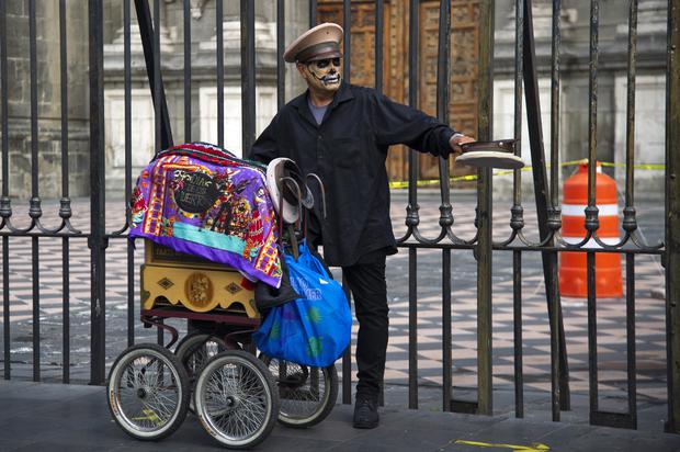 An organ grinder with a painted face asks for money in front of the Metropolitan Cathedral during the Day of the Dead celebrations in Mexico City.  (Photo: Photo by Claudio CRUZ / AFP).