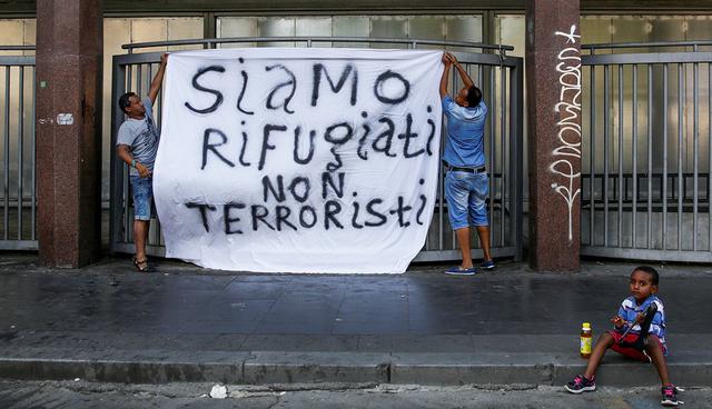 Refugees hang a banner reading "We are refugees, we aren't terrorists", after being forcibly removed from a building where they had been living, in central Rome, Italy, August 20, 2017. Picture taken August 20, 2017. REUTERS/Alessandro Bianchi