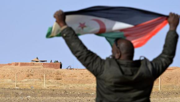 Hombre saharaui sostiene una bandera del Frente Polisario en el área de Al-Mahbes, cerca de los soldados marroquíes que custodian el muro que separa el Sahara Occidental controlado por Polisario. (Foto: AFP)