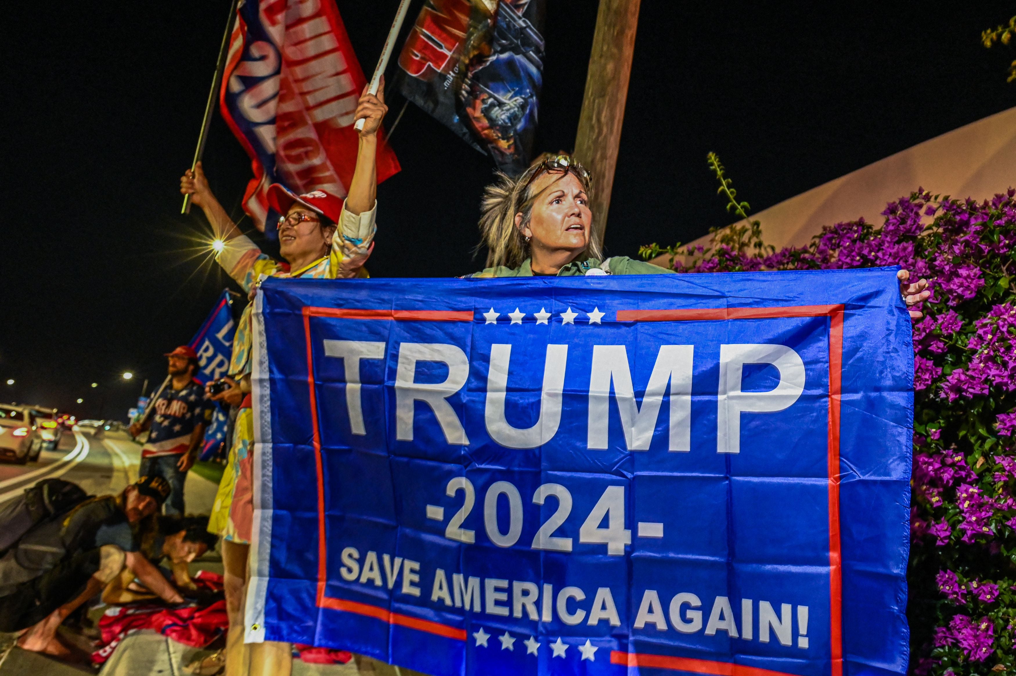 Supporters of Donald Trump hold flags in front of Trump's residence at Mar-A-Lago in West Palm Beach, Florida.  (Photo by Giorgio VIERA / AFP)