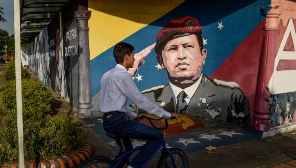 Un joven pasea en bicicleta frente a un mural que representa al fallecido presidente venezolano Hugo Chávez en su ciudad natal Sabaneta, estado de Barinas, Venezuela, el 27 de noviembre de 2018. (FEDERICO PARRA / AFP).
