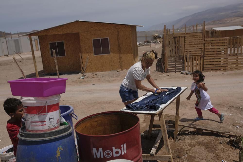 Venezuelan migrant Karla González washes clothes as her daughter runs outside the house her family built on occupied land in the La Mula neighborhood of Alto Hospicio, Chile.  (AP / Matias Delacroix)