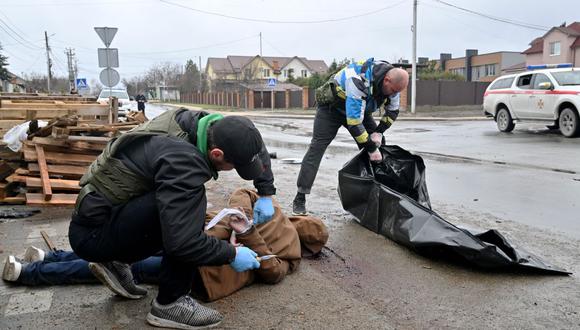 Un trabajador comunal corta la cuerda del cadáver de un hombre con las manos atadas a la espalda mientras otro prepara una bolsa de plástico para introducirlo en la ciudad de Bucha, cerca de Kiev, Ucrania, el 3 de abril de 2022. (SERGEI SUPINSKY / AFP).