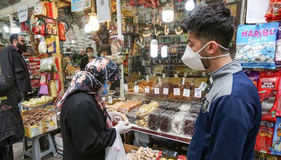 Una compradora vestido con una mascarilla y guantes de látex, debido a la pandemia del coronavirus COVID-19, inspecciona el jengibre en un comerciante de especias en Tajrish Bazaar en la capital de Irán, Teherán. (Foto: ATTA KENARE / AFP)