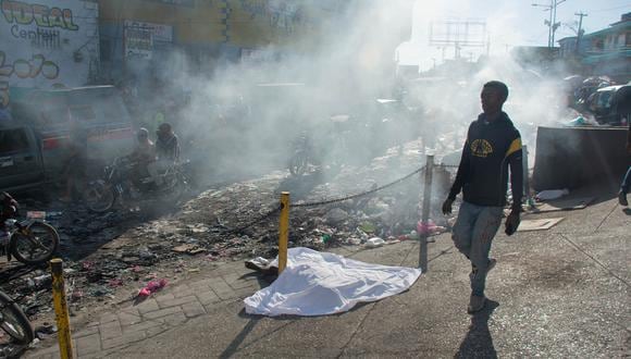 Un hombre pasa junto al cuerpo de una persona que estaba entre una docena asesinada en la calle por pandilleros, en Petionville, Puerto Príncipe, Haití, el 18 de marzo de 2024. (Foto de Clarens SIFFROY / AFP)