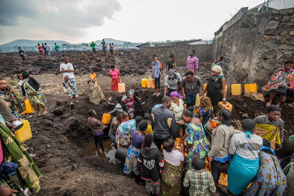 Un grupo de residentes se reúne alrededor de un punto de agua con bidones amarillos en un campo cubierto de lava, en Goma, ciudad del este de la República Democrática del Congo, angustiada este martes por una nueva erupción del volcán Nyiragongo. (Moses Sawasawa / AFP).