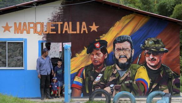 Un hombre y niños junto a un grafiti del difunto comandante de las FARC Alfonso Cano (C) en el Área Territorial de Capacitación y Reincorporación (ETCR) El Oso, en Gaitania, Departamento de Tolima, Colombia. (RAUL ARBOLEDA / AFP).