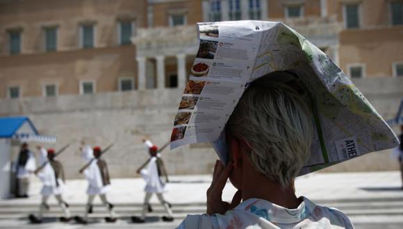 Una mujer se cubre la cabeza con un volante turístico de Atenas para protegerse del sol mientras la Guardia Presidencial griega actúa durante una ola de calor en el centro de Atenas, Grecia. (Foto: EFE / EPA / YANNIS KOLESIDIS).