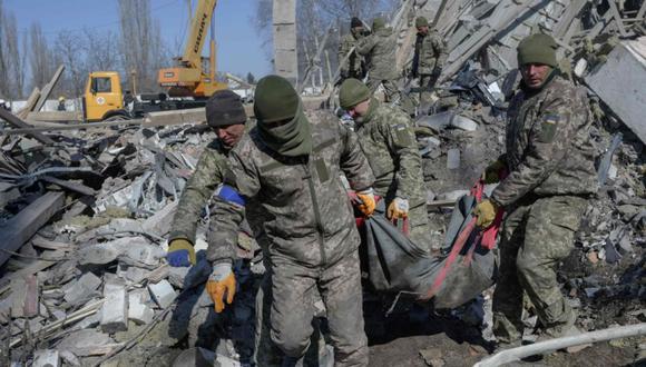 Soldados ucranianos cargan a un soldado muerto a través de los escombros en la escuela militar alcanzada por cohetes rusos el día anterior, en Mykolaiv, sur de Ucrania. (Foto: BULENT KILIC / AFP)