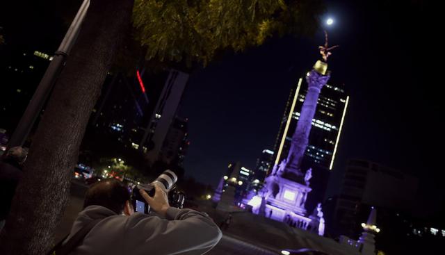 Un hombre está tomando fotos de la Súper Luna durante el inicio del eclipse lunar total, en el Ángel de la Independencia en la Ciudad de México. (Foto: AFP)