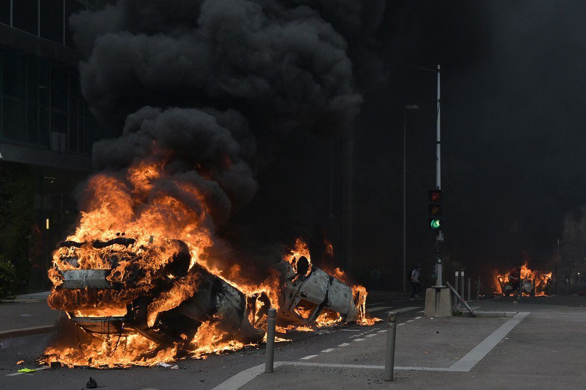 A photograph shows burning cars in the street at the end of a commemoration march for a teenage driver shot dead by a police officer, in the Paris suburb of Nanterre, on June 29, 2023. (Photo by Alain JOCARD / AFP)
