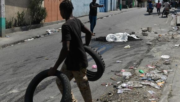 Transeúntes pasan junto al cadáver calcinado de una persona en la calle, el 20 de marzo de 2024, en Puerto Príncipe, Haití. (Foto de Johnson Sabin / EFE)