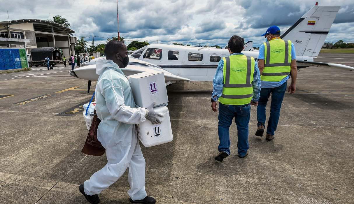 Fotografía de un trabajador de la salud llevando cajas con pruebas COVID-19 a un avión que se dirige a Bogotá desde Quibdó. (AFP / Juan BARRETO).