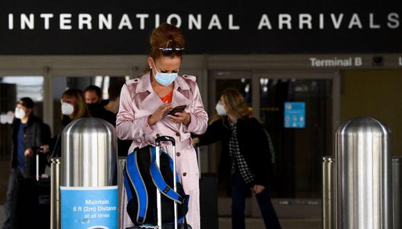 Una viajera usa mascarilla facial mientras revisa su teléfono en el Aeropuerto Internacional de Los Ángeles (LAX), Estados Unidos, en medio de la pandemia de coronavirus. (PATRICK T. FALLON / AFP).