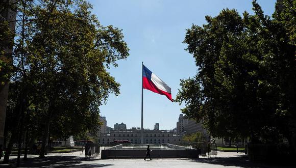 Un hombre pasa frente a un asta con la bandera de Chile en un parque frente al Palacio de la Moneda. El país tendrá un fin de semana de megacuarentena, con el 97 % de la población confinada. (EFE/Alberto Valdés).