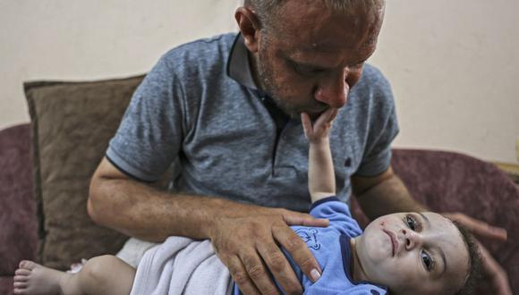 Mohammad al-Hadidi en la casa de su hermano sosteniendo a su hijo Omar, quien fue sacado con vida de debajo de los escombros mientras su madre y cuatro hermanos murieron en un ataque aéreo israelí en Gaza. (Foto de MAHMUD HAMS / AFP).