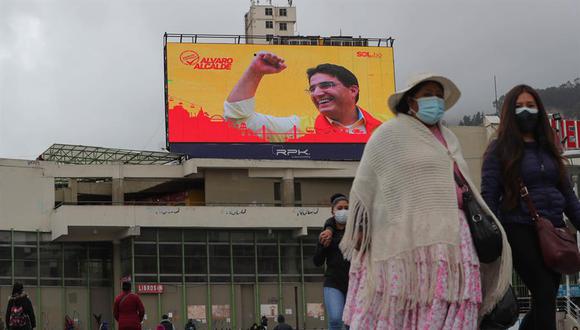 Varias personas caminan frente a una pantalla gigante de publicidad electoral en La Paz (Bolivia). El Movimiento al Socialismo (MAS) del presidente boliviano, Luis Arce, y del exmandatario Evo Morales libra una nueva batalla en medio de la pandemia de la COVID-19 ante una oposición política disgregada a un mes de los comicios subnacionales. (EFE/ Martín Alipaz)