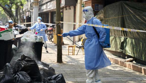 Un trabajador con equipo de protección desinfecta una pila de bolsas de basura en Shanghái.