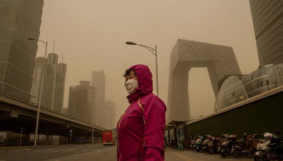 Una mujer espera en una parada de autobús durante una tormenta de arena en el distrito financiero de Beijing el 15 de marzo de 2021. (Foto de NICOLAS ASFOURI / AFP).
