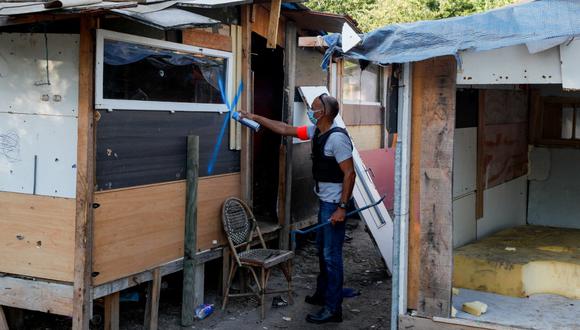 Un oficial de policía pinta una cruz azul en las casas que serán demolidas, luego de la evacuación de miembros de la comunidad romaní y migrantes de un barrio pobre en Vitry-sur-Seine, suburbios del sureste de París, el pasado 20 de agosto de 2020. (GEOFFROY VAN DER HASSELT / AFP)