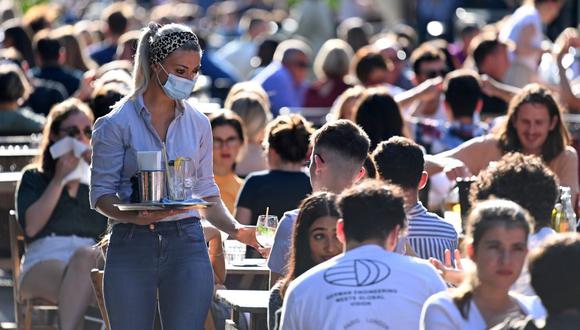 Una camarera que usa mascarilla protectora lleva bebidas a los clientes en las mesas al aire libre en Soho, en el centro de Londres, el 20 de septiembre de 2020, en pleno repunte del coronavirus. (Foto de DANIEL LEAL-OLIVAS / AFP).