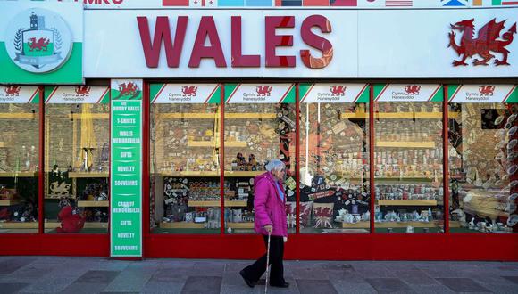 Una mujer que usa una visera protectora pasa frente a una tienda de souvenirs que vende artículos de temática galesa, en Cardiff, Gales del Sur. (Foto de Geoff Caddick / AFP).
