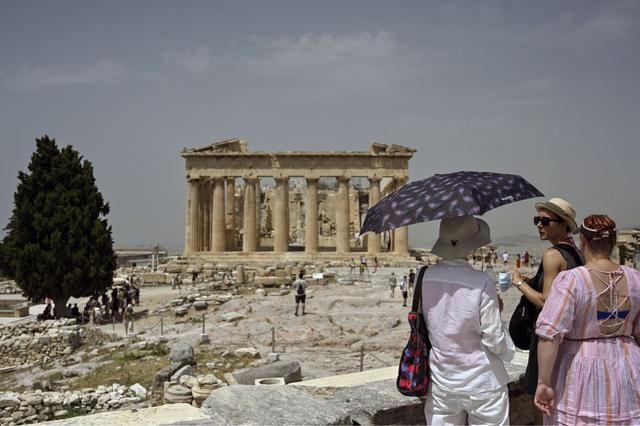 Una turista sostiene una sombrilla mientras visita el sitio arqueológico de la antigua Acrópolis en Atenas (Grecia), el 1 de julio de 2021. (Louisa GOULIAMAKI / X07402 / AFP).