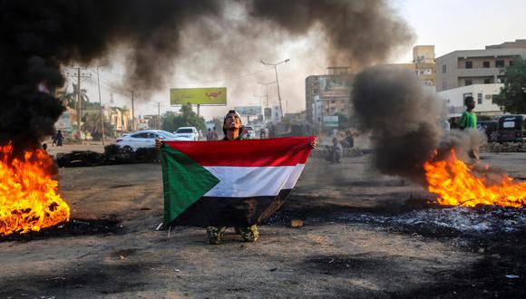Un manifestante sudanés sostiene la bandera nacional junto a neumáticos en llamas durante una manifestación en la capital, Jartum, el 26 de octubre de 2021. (EFE / EPA / MOHAMMED ABU OBAID).