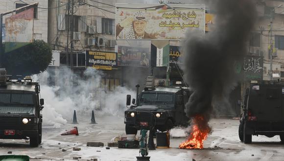 El humo blanco del gas lacrimógeno disparado por tropas de Israel se esparce detrás de neumáticos quemados en una calle con barricadas en la ciudad ocupada de Tulkarem, en Cisjordania, el 14 de noviembre de 2023. (Foto de Jaafar ASHTIYEH / AFP).