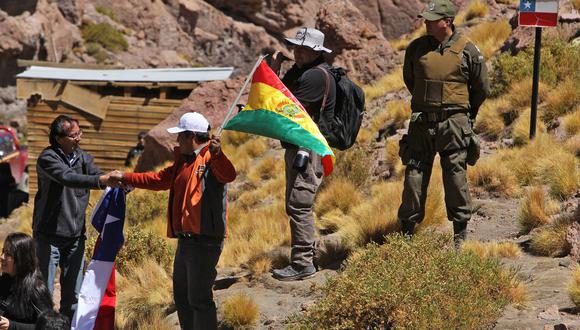 En esta foto de archivo tomada el 29 de marzo de 2016, un chileno (izquierda) y un boliviano con sus banderas nacionales se dan la mano en la frontera entre Bolivia y Chile visto desde el departamento de Potosí, Bolivia.
