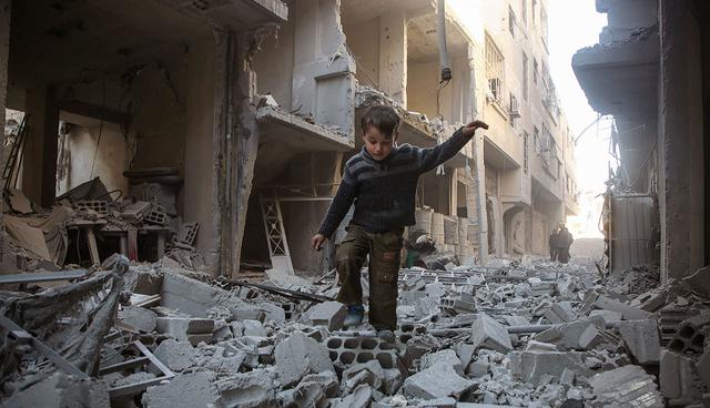 TOPSHOT - A Syrian boy walks through a street covered with rubble from a heavily damaged building following air strikes by regime forces in Arbin, in the rebel-held Eastern Ghouta region on the outskirts of the Syrian capital Damascus, on February 1, 2018. Arbin is in the Eastern Ghouta region which has been under government siege since 2013. / AFP / Amer ALMOHIBANY