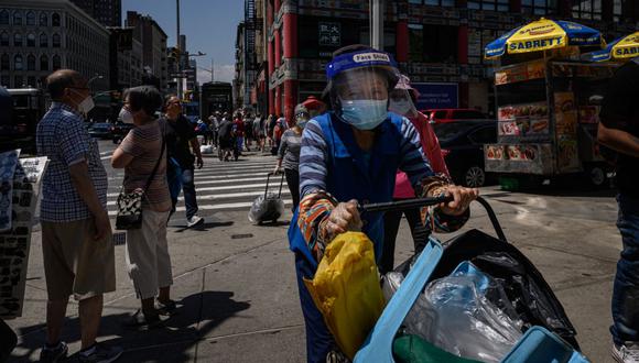 Una mujer con mascarilla y protector facial empuja un carrito por una calle de Nueva York el 15 de junio de 2022. (Foto de Ed JONES / AFP)