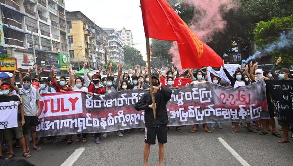 Los manifestantes sostienen una pancarta que dice "Lucha manteniendo el espíritu del 7 de julio en alto, destruye la dictadura desde la raíz por todos los medios" mientras otro sostiene la bandera de la Unión de Estudiantes de Myanmar durante una protesta. Manifestación contra el golpe militar en Yangon. (Foto por AFP)